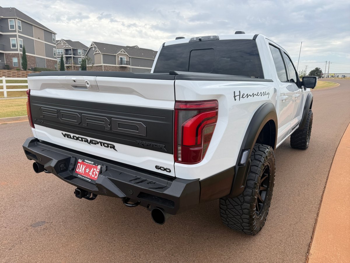 White Ford VelociRaptor pickup truck parked in a residential driveway, showing rear three-quarter view with lifted suspension